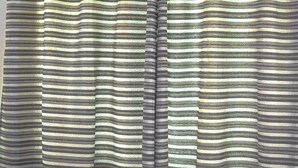 A window with a striped curtain and an air conditioning unit above it.