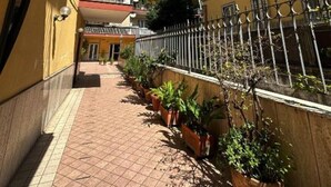 A narrow outdoor corridor with tiled flooring, potted plants, and a metal fence. - 2 bedroom apartment in naples (Napoli)