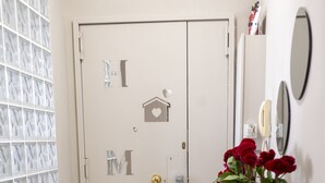 A hallway with a double door, a small wooden table with a vase of red flowers, and a window with patterned curtains. - 2 bedroom apartment in naples (Napoli)