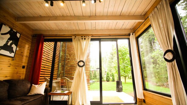 Una habitación acogedora con techo de madera, un sofá, una mesita y un amplio ventanal corredero que da a un jardín.