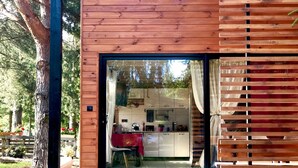 Una cabaña de madera con un cerramiento de vidrio corredera que da a una zona de cocina con armarios blancos y mantel rojo.