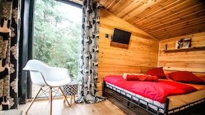Una habitación de cabaña de madera con una cama, una silla y un ventanal con cortinas.