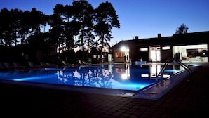 Una piscina al anochecer con sillones de descanso y un edificio al fondo.