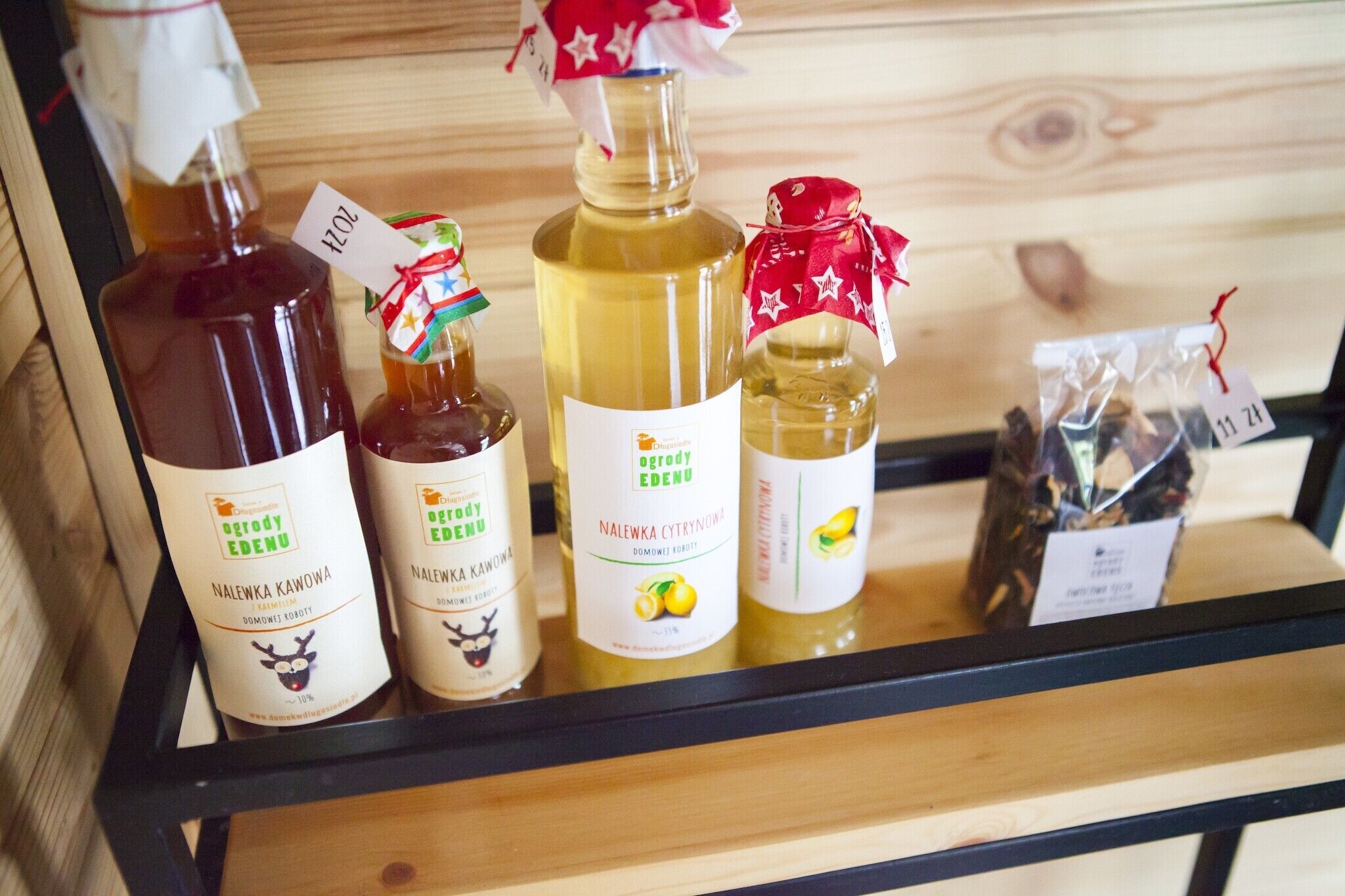 A wooden shelf with bottles of 'Nalewka Kawowna' and 'Nalewka Cytrynowa' on a black metal rack.