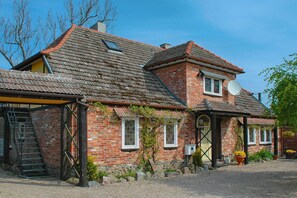 A two-story brick house with a tiled roof, a satellite dish, and a small garden area with potted plants.