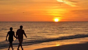 A sunset over the ocean with silhouettes of two people walking on the beach.