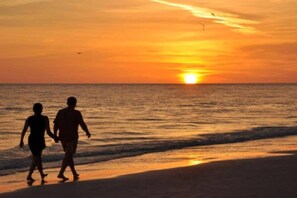 A sunset over the ocean with silhouettes of two people walking on the beach.