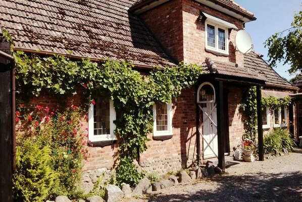 A traditional brick house with a sloped roof, a satellite dish, and a small garden with various plants and flowers.