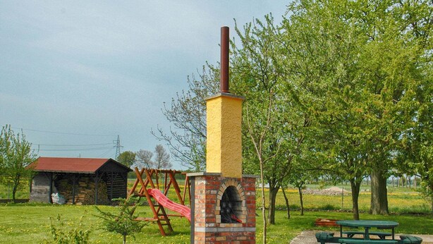 A brick oven structure with a chimney, a playground with a slide, and a picnic table in a grassy area.