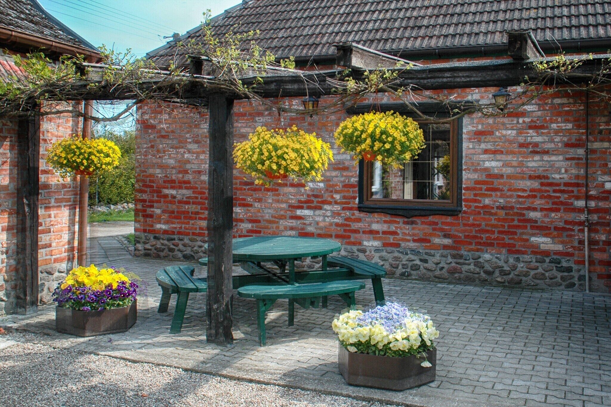 A brick building with a tiled roof, a green picnic table, and hanging flower baskets.