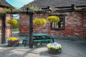 A brick building with a tiled roof, a green picnic table, and hanging flower baskets.