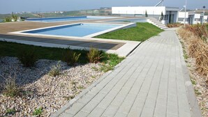 A modern outdoor pool area with multiple pools, a paved walkway, and a building with satellite dishes. - Villa in Portugal with Sea View & Pool (Lourinhã)