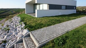 A modern building with a flat roof, large windows, and a paved pathway leading to it. - Villa in Portugal with Sea View & Pool (Lourinhã)
