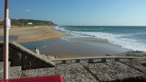 A beach with a stone staircase leading down to the water, a red umbrella, and a view of the ocean. - Villa in Portugal with Sea View & Pool (Lourinhã)