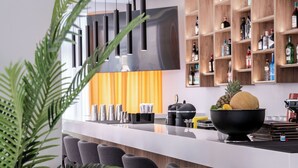 A modern kitchen with a central island, bar stools, a coffee machine, and a fruit bowl.