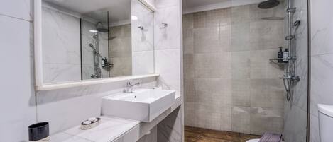 A modern bathroom with a large mirror, two sinks, a shower, and a toilet.