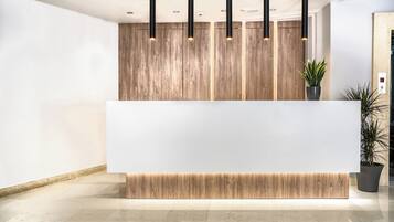 A modern reception desk with a wooden panel backdrop, black pendant lighting, and a potted plant.