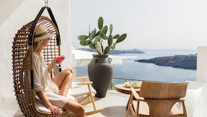 A woman sitting on a hanging chair on a balcony overlooking a scenic view.