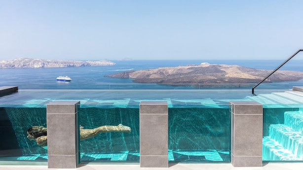 A clear view of a swimming pool with a glass bottom, a person swimming, and a distant island.