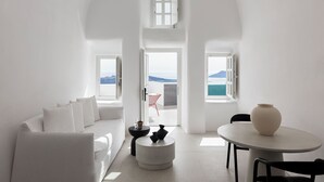 A modern, white interior with a sofa, a round table, and a view of the sea.