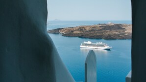 A view through a doorway of a white building overlooking a calm sea with a cruise ship.