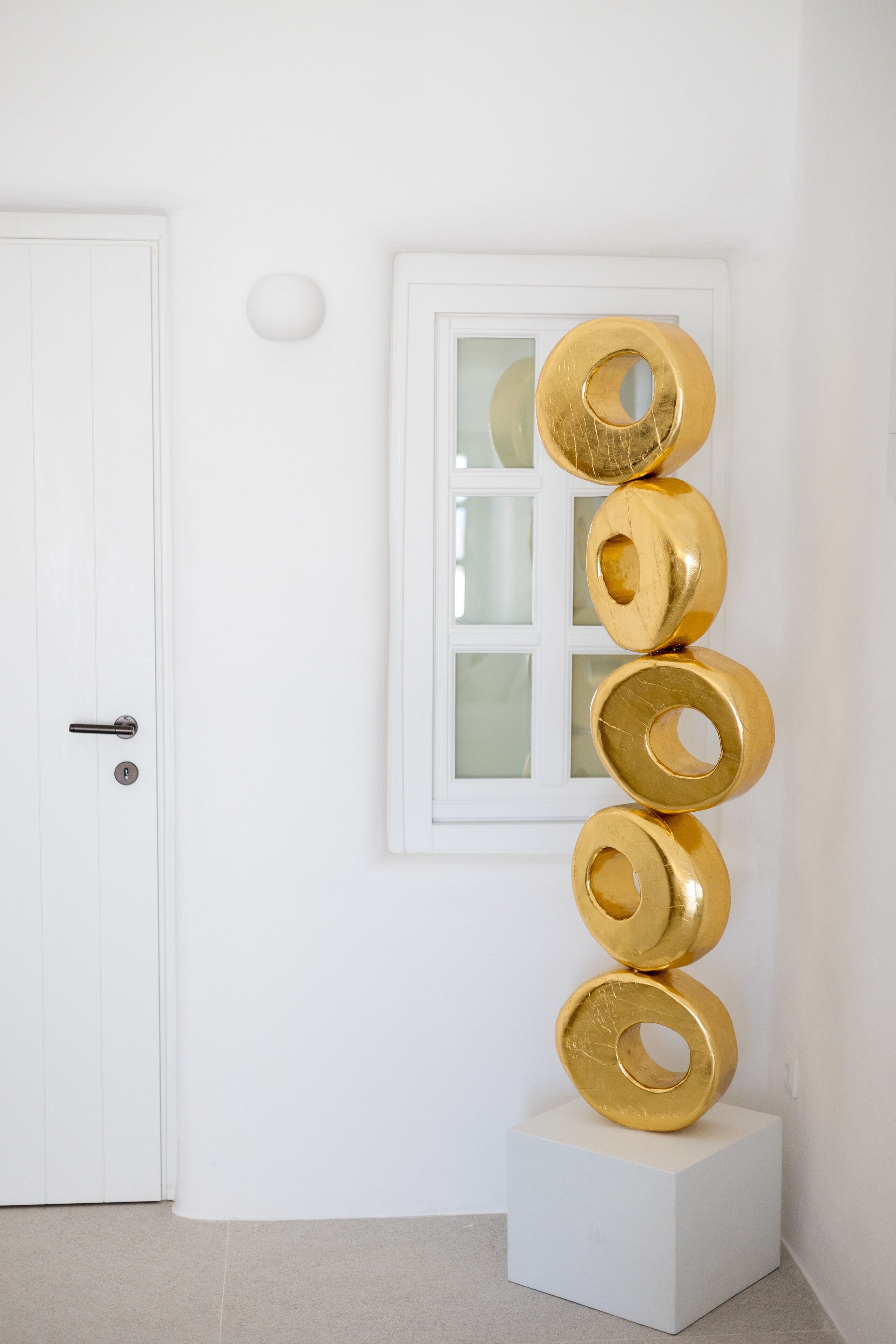 A white door with a keyhole, a white wall with a window, and a white pedestal with a gold sculpture.