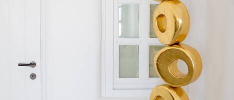 A white door with a keyhole, a white wall with a window, and a white pedestal with a gold sculpture.