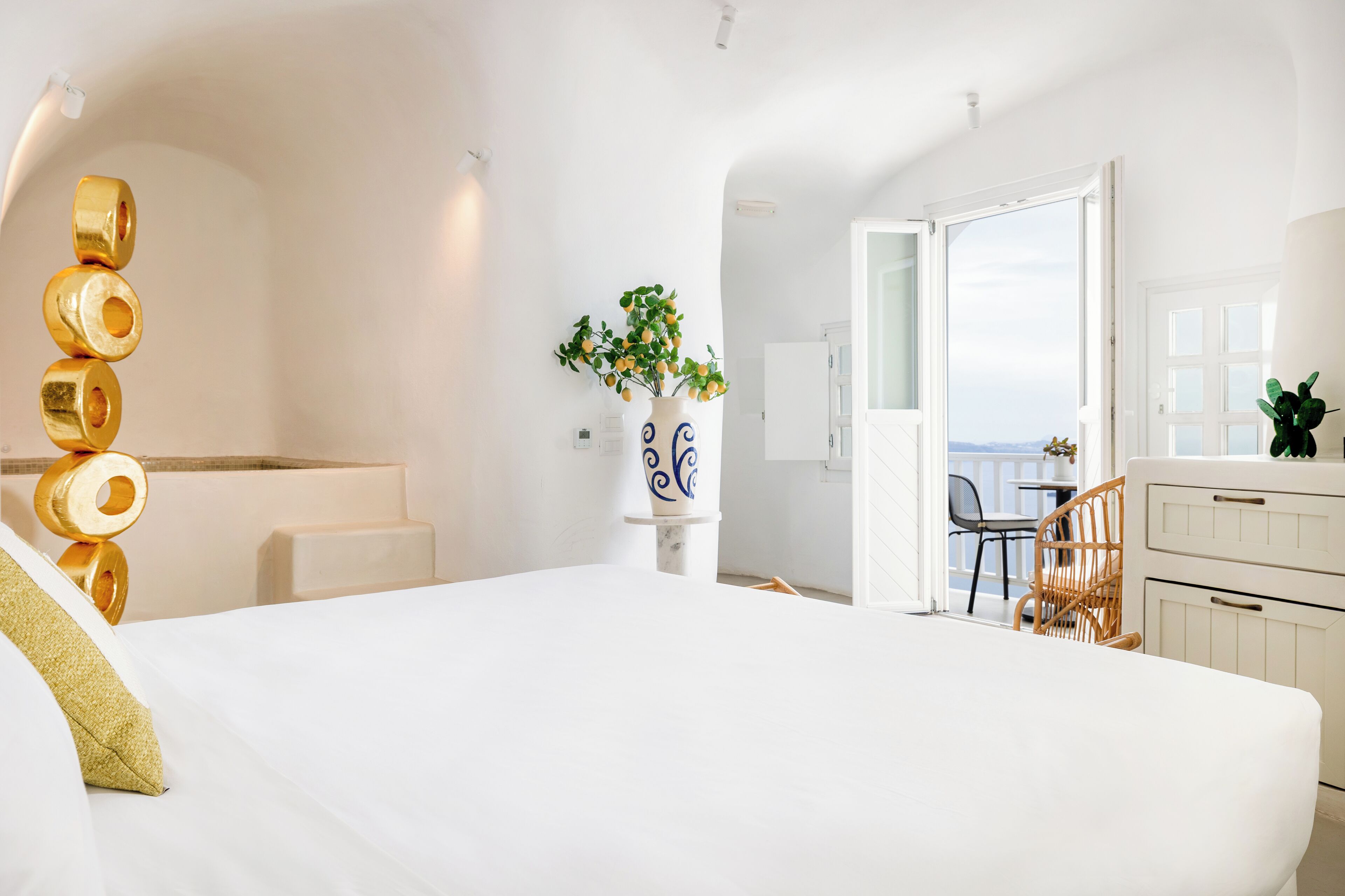 A hotel room with a large bed, a bathroom with a white vanity, and a view of the sea through an open door.