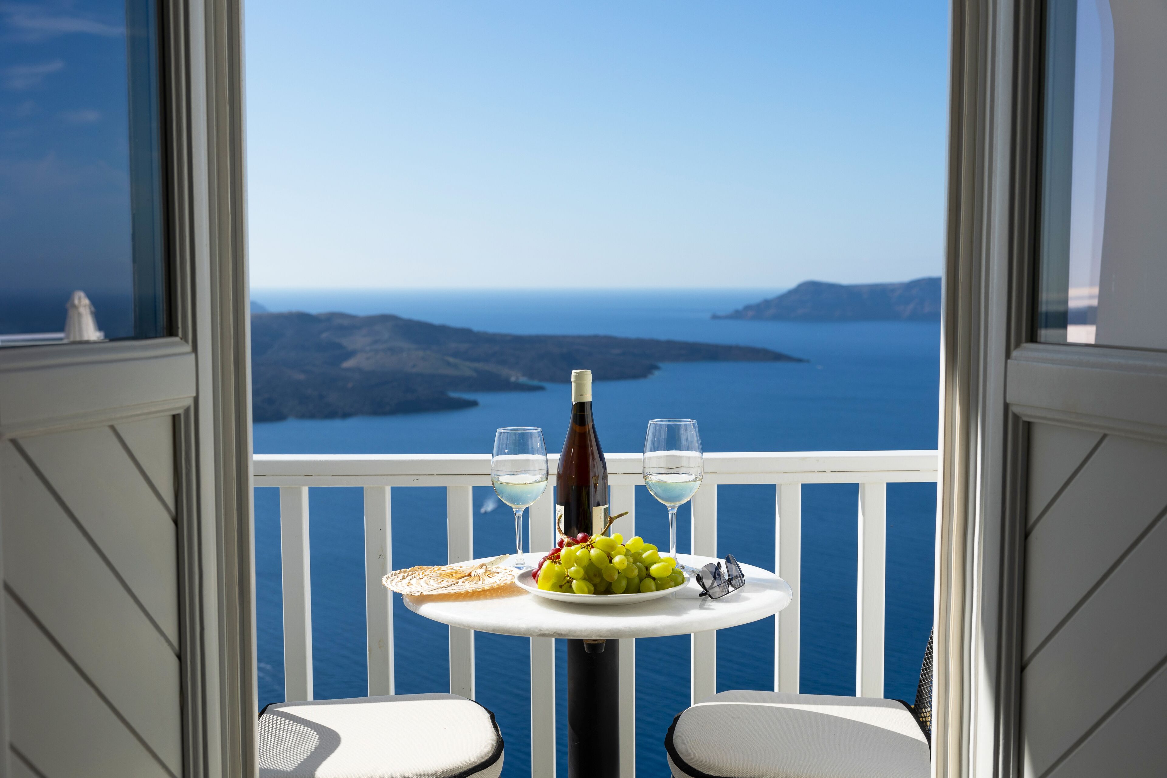 A balcony with a table set for two, featuring a bottle of wine, two glasses, a plate of grapes, and a napkin.