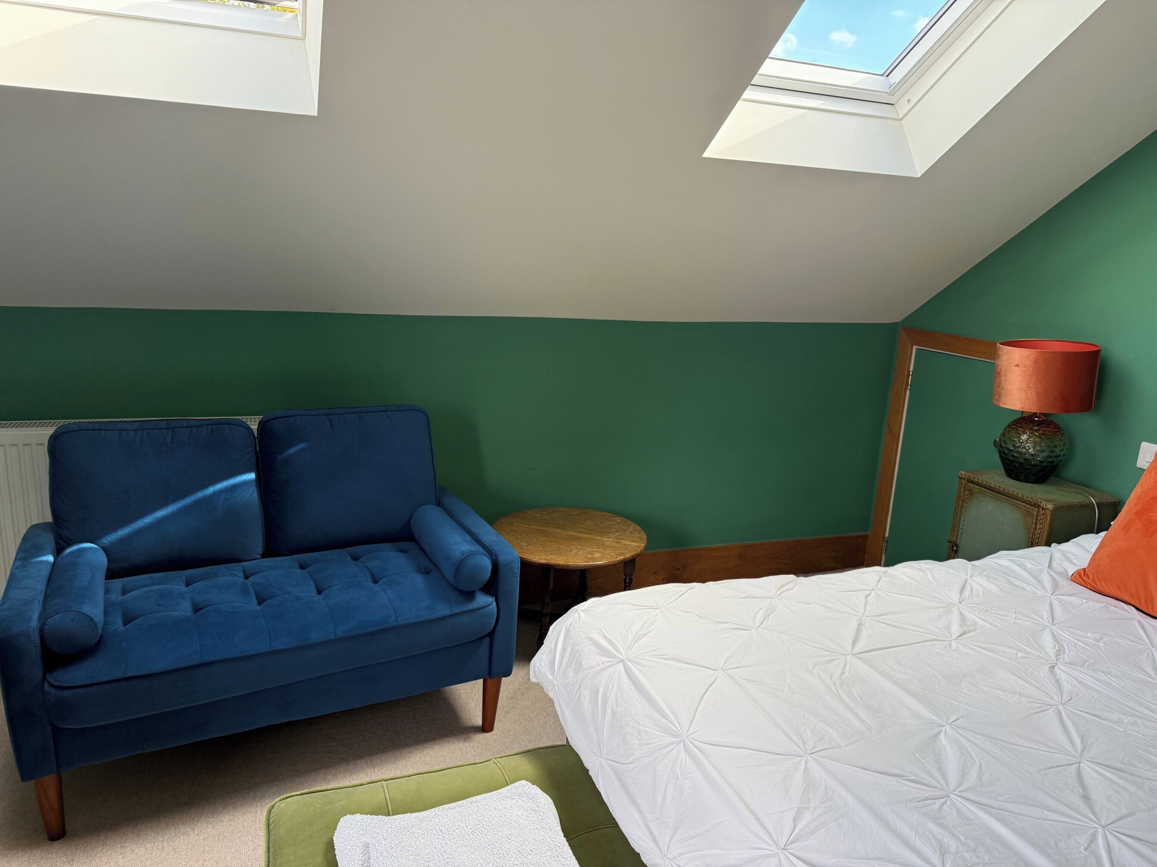 A bedroom with a blue sofa, a white bed, a small round table, and a lamp.