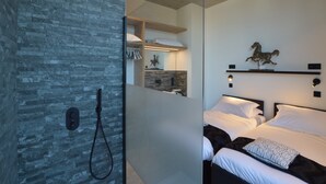 A modern bedroom with a large bed, a shower area, and a stone wall. - Modern Dalhem Villa with Views (Dalhem)