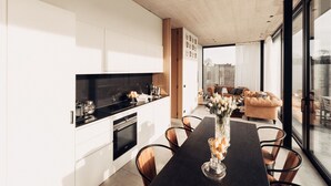 A modern kitchen with white cabinets, a black countertop, and a dining area with a black table and chairs. - Modern Dalhem Villa with Views (Dalhem)