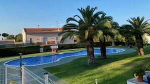 A swimming pool surrounded by palm trees and a building with a tiled roof. - Tranquilo Apartamento con Vistas al mar y Piscina en Cap Salou (CT)