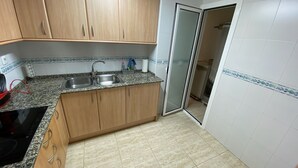 A kitchen with wooden cabinets, a granite countertop, a double sink, and a tiled backsplash. - Tranquilo Apartamento con Vistas al mar y Piscina en Cap Salou (CT)