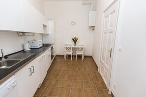 A compact kitchen with white cabinets, a black countertop, and a brown tiled floor.
