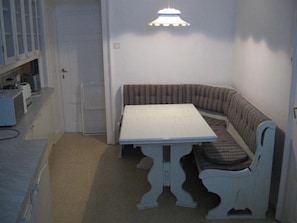 A small, compact room with a white table and bench, a kitchenette area, and a door.