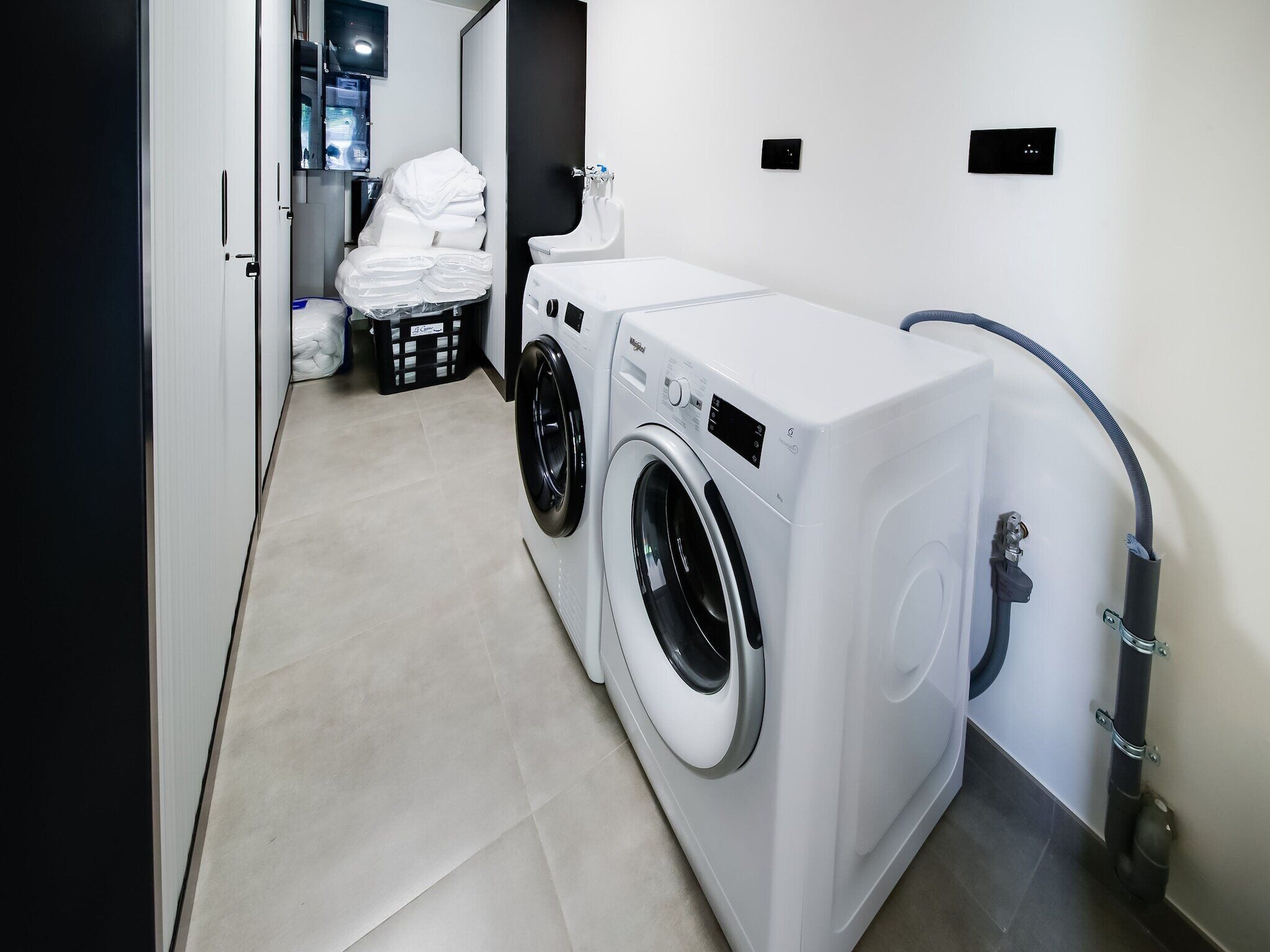 A laundry area with a front-loading washing machine and dryer, a small trash bin, and neatly folded towels on a rack.