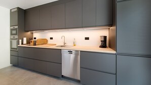 Una cocina moderna con armarios grises, lavavajillas de acero inoxidable y una cafetera.