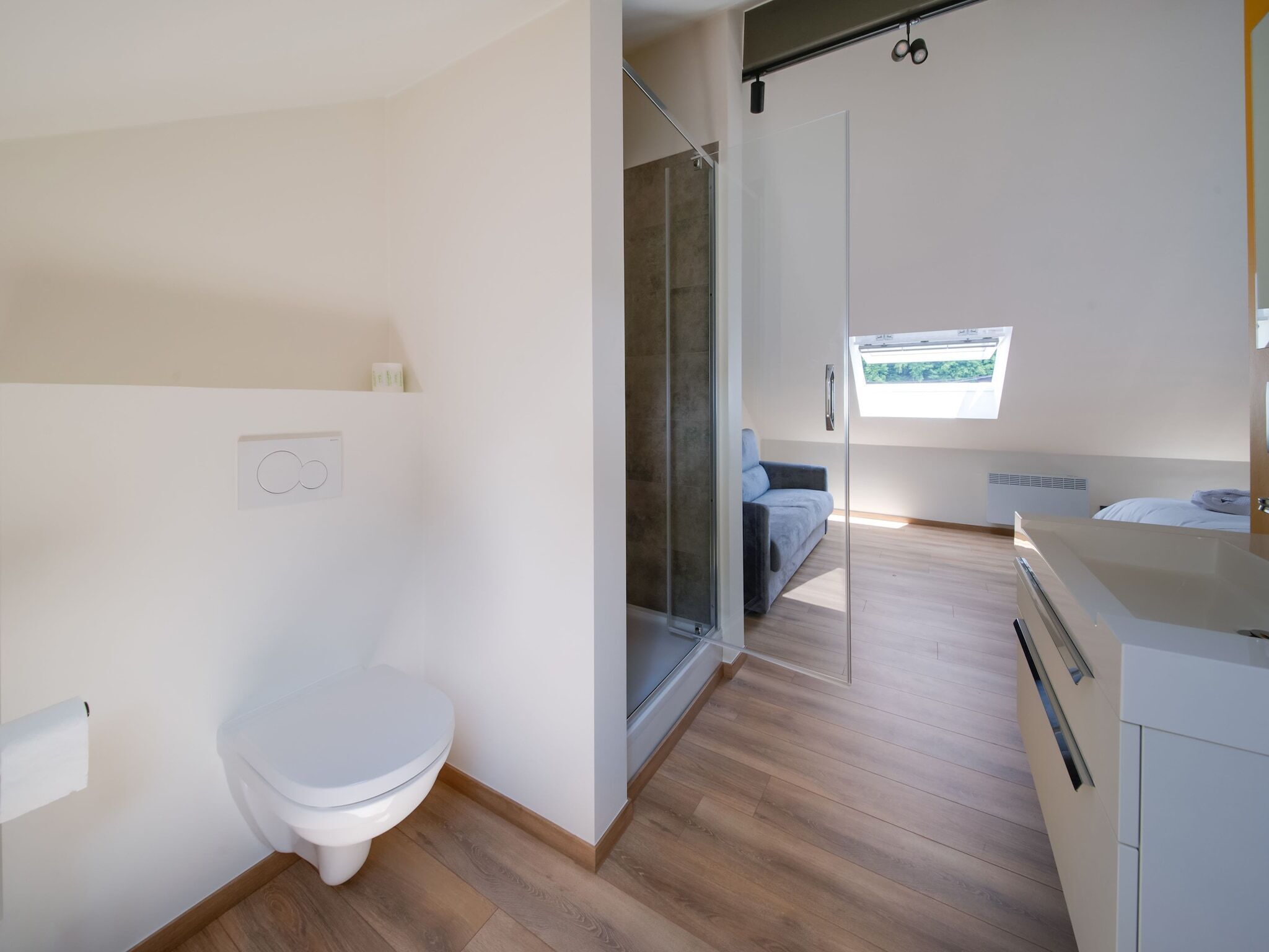 Une salle de bain moderne comprenant des toilettes, un espace douche et une porte en verre donnant sur une chambre.
