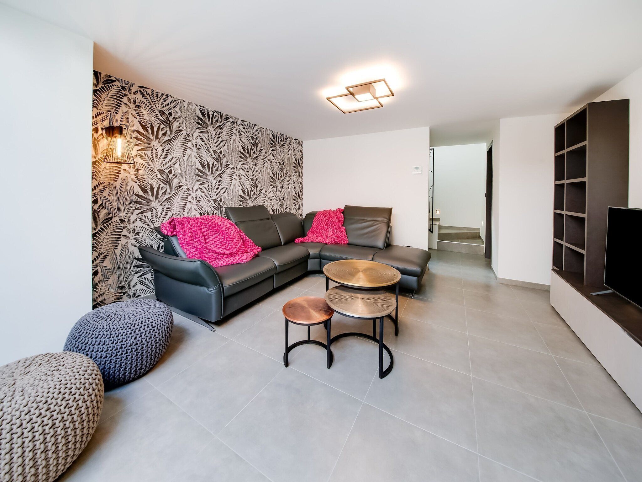 A modern living room with a black leather sofa, two round coffee tables, and a patterned wallpaper.