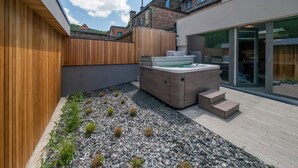 Un patio moderno al aire libre con jacuzzi, terraza de madera y zona de jardín con grava.
