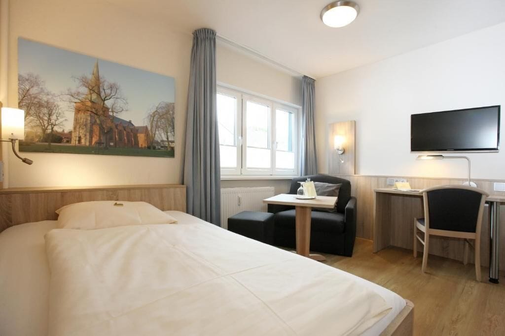 Et hotelværelse med seng, skrivebord, stol, fjernsyn og et billede på væggen.