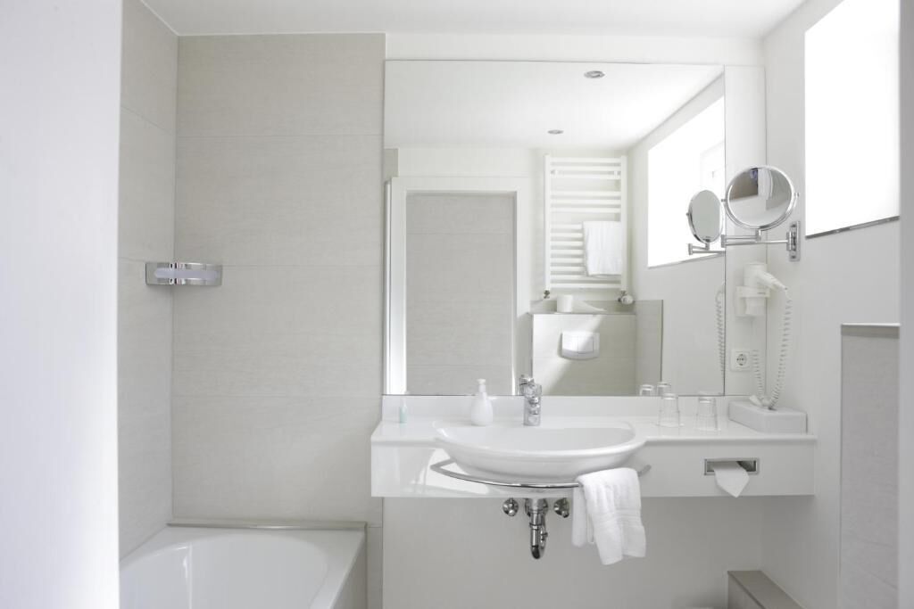 A modern bathroom with a white sink, mirror, and bathtub.