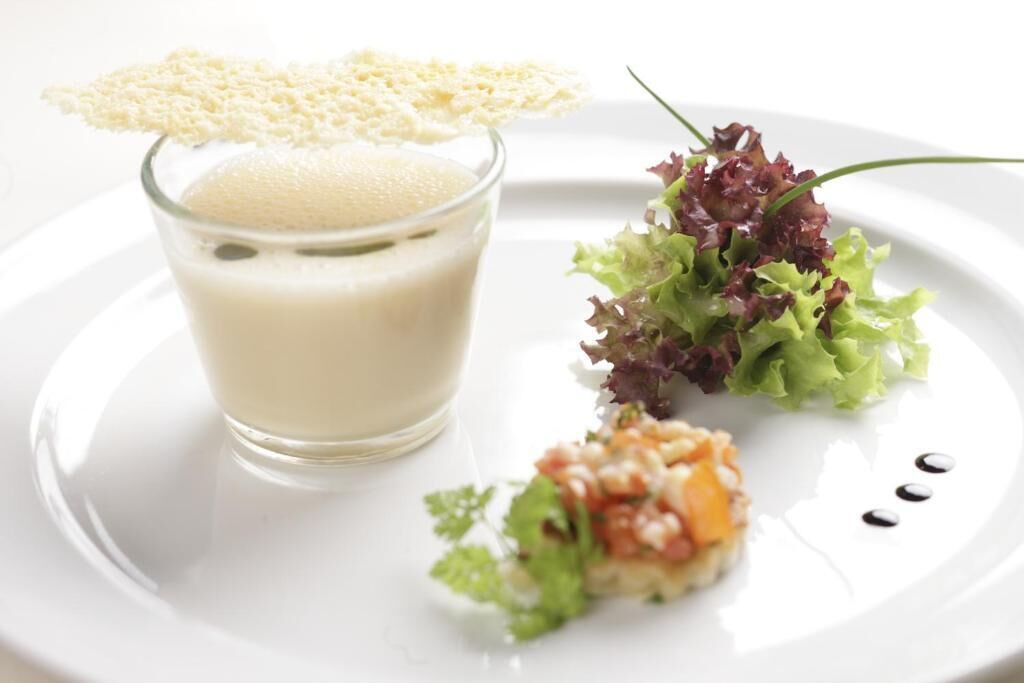 Ein Glas weißes Getränk mit cremiger Textur, dazu ein kleiner Salat und eine Garnitur auf einem weißen Teller.