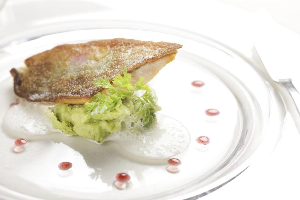 Um prato com um pedaço de comida, possivelmente peixe, e alguns enfeites verdes.