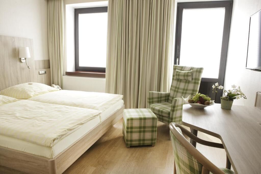 Een hotelkamer met een bed, een stoel, een klein tafeltje met een schaal fruit en een bloempot.