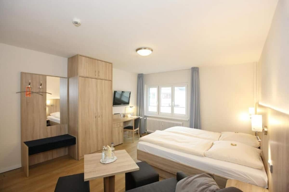 A hotel room with a bed, a desk, a TV, and a wardrobe.