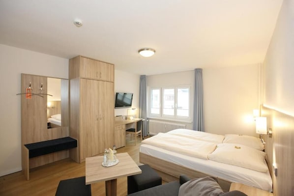 Una habitación de hotel con una cama, un escritorio, un televisor y un armario.