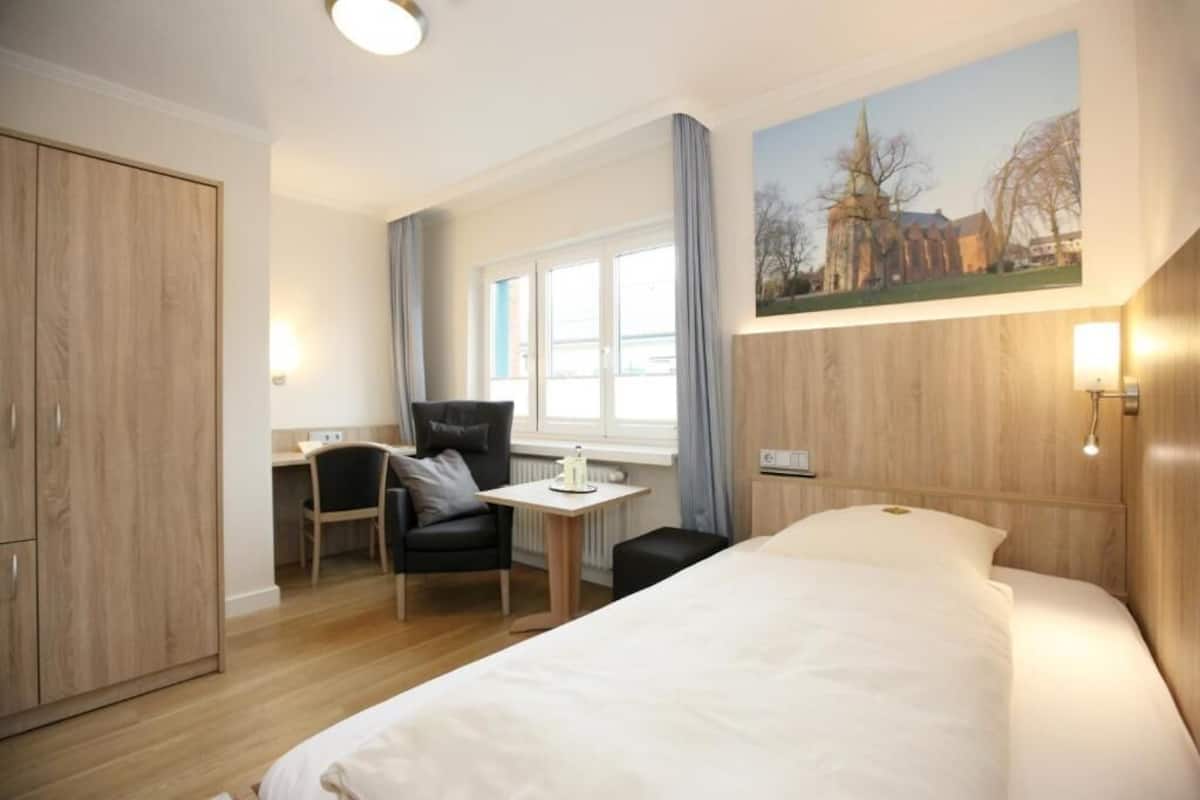 A hotel room with a bed, a desk, a chair, and a window with curtains.