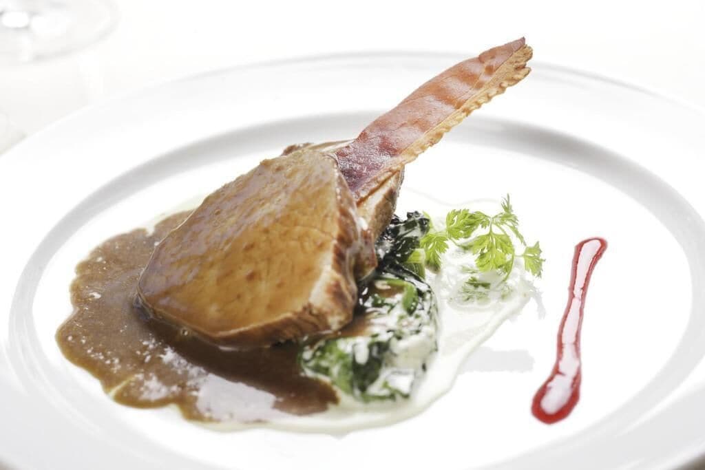 Une assiette contenant une côte d’agneau, des légumes verts et une sauce.